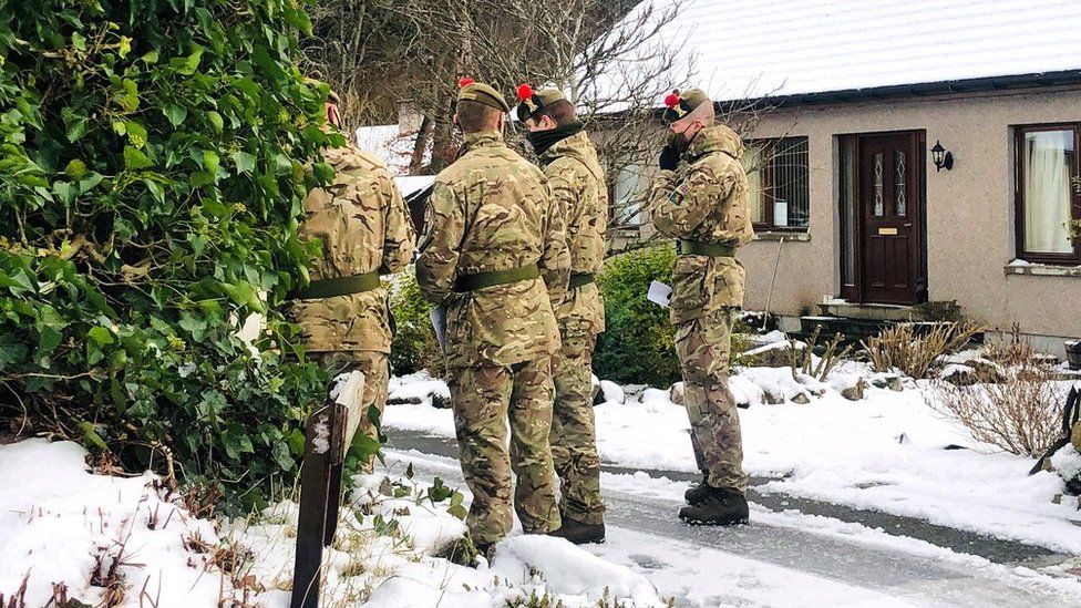 Army troops in the snow outside a house