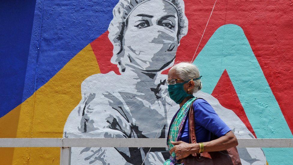 An elderly woman wearing a mask walks past a mural on Covid-19 in Mumbai.