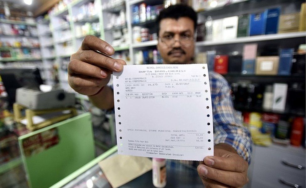 Владелец магазина показывает новый обновленный счет GST возле магазина в Connaught Place 1 июля 2017 года в Нью-Дели, Индия