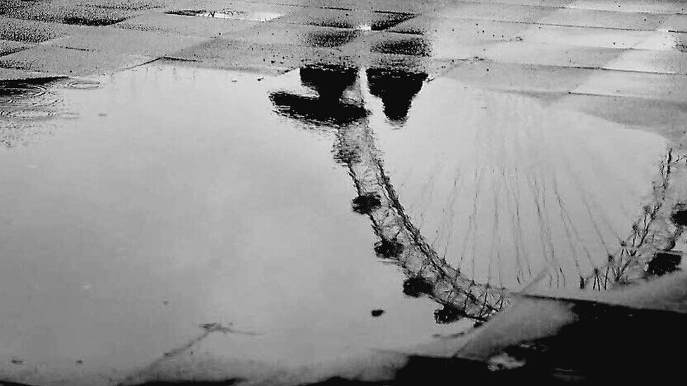 Reflection of two people and London Eye in a puddle