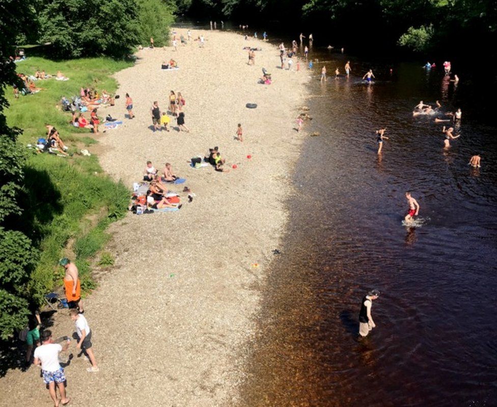 People on a river bank with some getting into the water