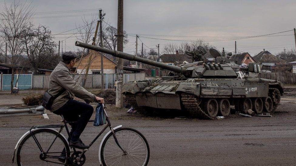 A man rides his bike past a destroyed Russian tank on 30 March, 2022 in Trostyanets, Ukraine.