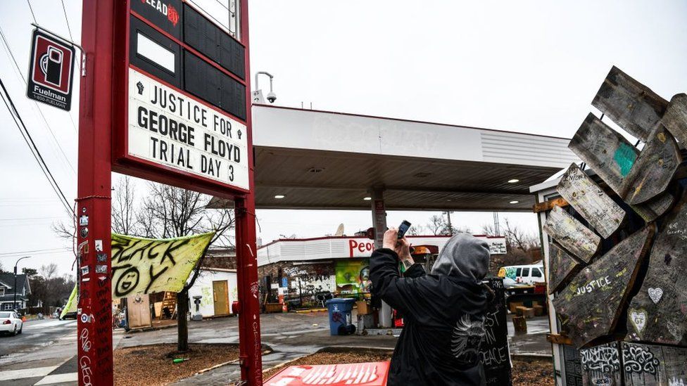 People take photo of gas station signage across the makeshift memorial of George Floyd before the third day of jury selection begins in the trial of former police officer Derek Chauvin