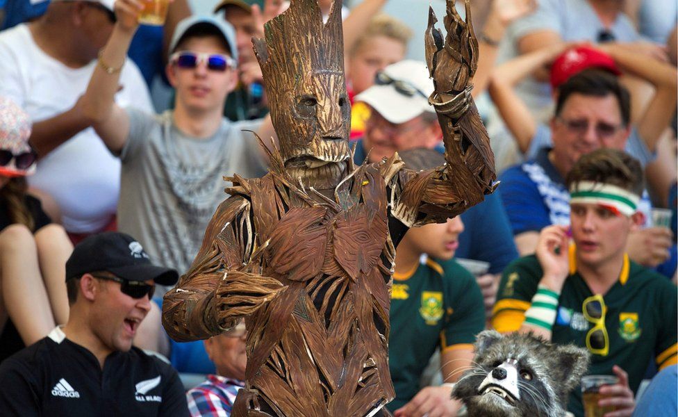 Two persons dressed as Groot (L) and Rocket Raccoon from Guardians of the Galaxy react during the World Rugby Sevens Series semi-final match England vs Scotland, on December 11, 2016, in Cape Town