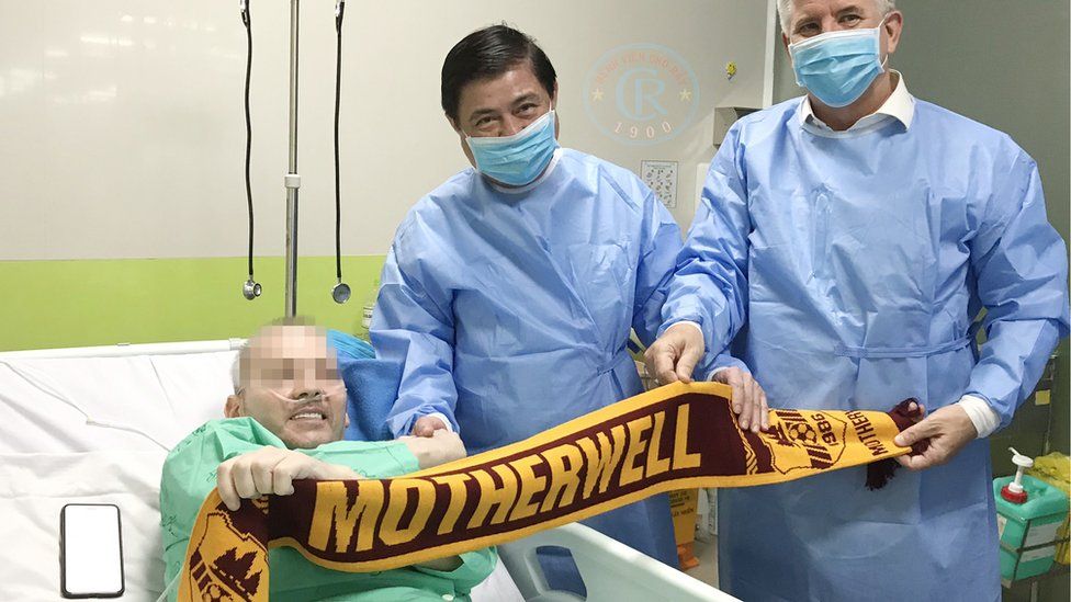 Stephen Cameron, face blurred, poses with a Motherwell scarf in hospital
