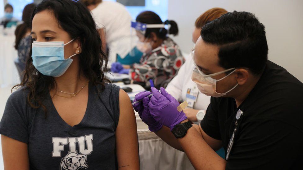 Камила Гутьеррес, студентка Международного университета Флориды, получает вакцину Pfizer-BioNtech COVID-19 от Джейсона Родригеса, студента-фармацевта, в больнице Jackson Memorial Hospital 15 апреля 2021 года в Майами, Флорида
