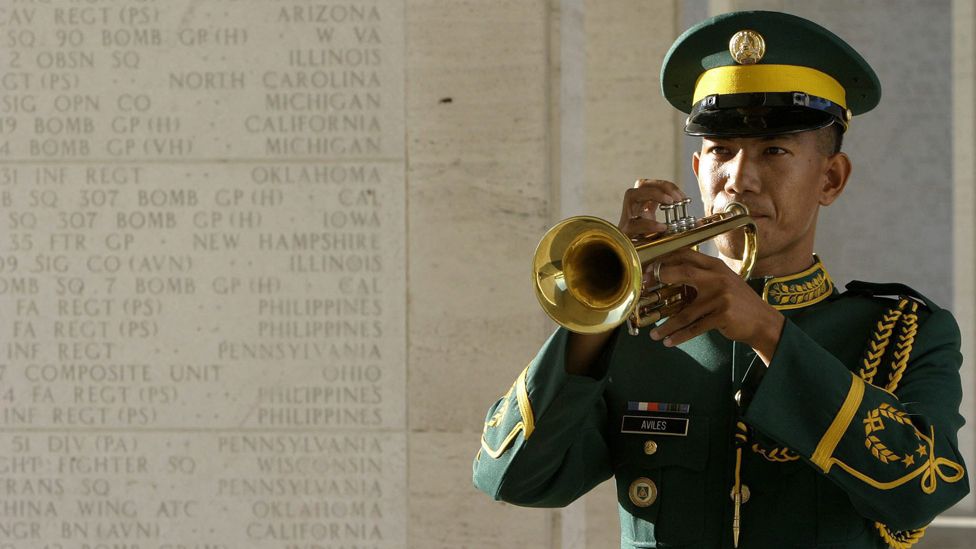 A Philippine army bugler plays beside a wall inscribed with names of fallen Filipino and American soldiers during a Memorial Day service at the American Cemetery in Manila, Philippines, on Monday, 31 May 2004