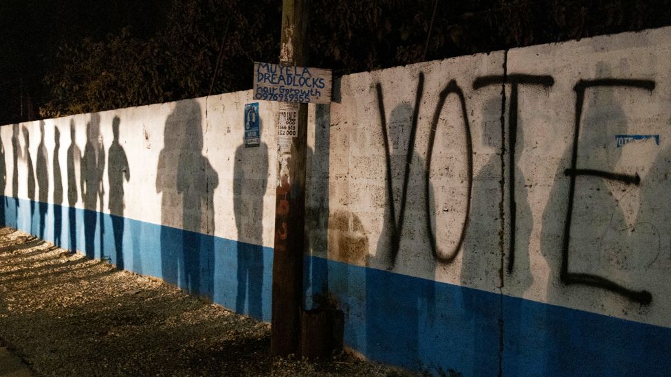 The silhouettes of people queueing up to vote seen on a wall with the word "Vote" painted on it - Thursday 12 August 2021