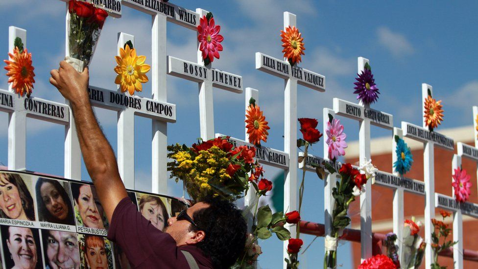 A relative of victims of the Casino Royale puts flowers on a cross during the commemoration of the first anniversary of the crime in Monterrey