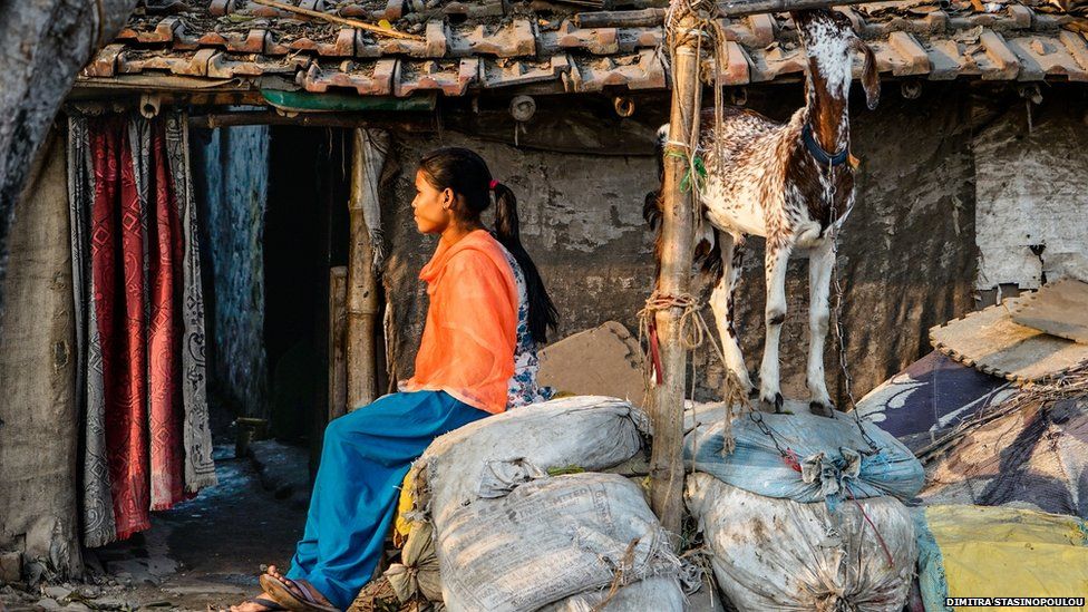 A young woman sitting outside a small building in a slum in Kolkata.