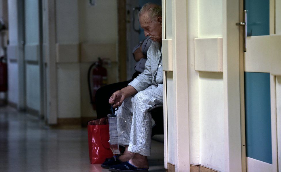 An elderly man looks dejected as he waits in a Greek hospital
