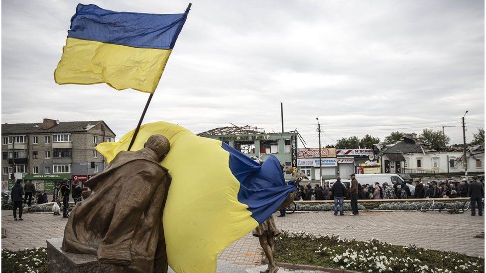 Ukrainian flag waves in front of statue in Kharkiv region