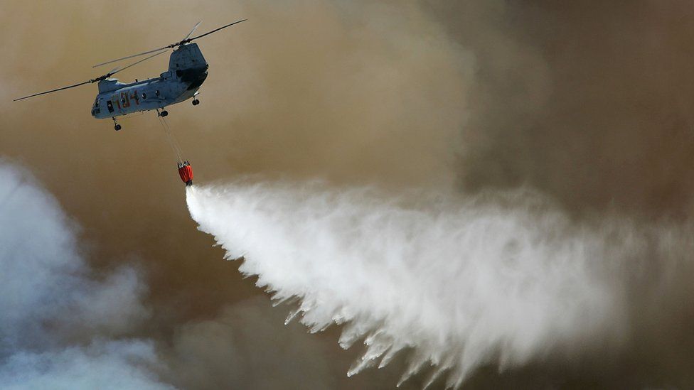 Вертолет пролетает над лесным пожаром, сбрасывая воду