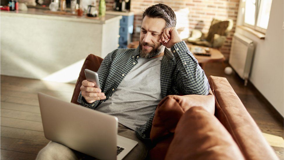 Stock image of man on laptop and using smartphone