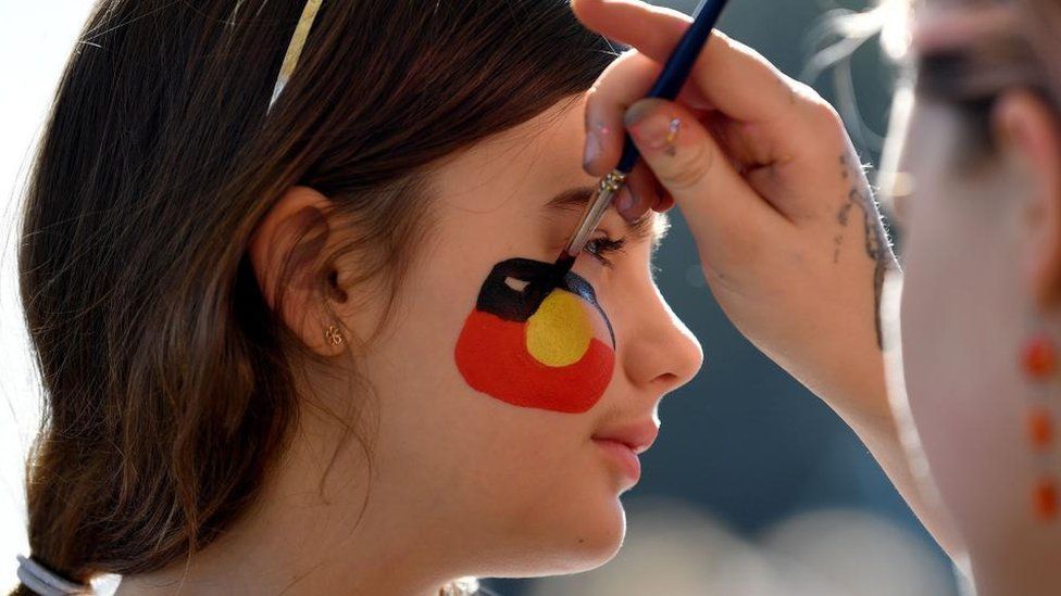 A girl has the Aboriginal flag painted on her face