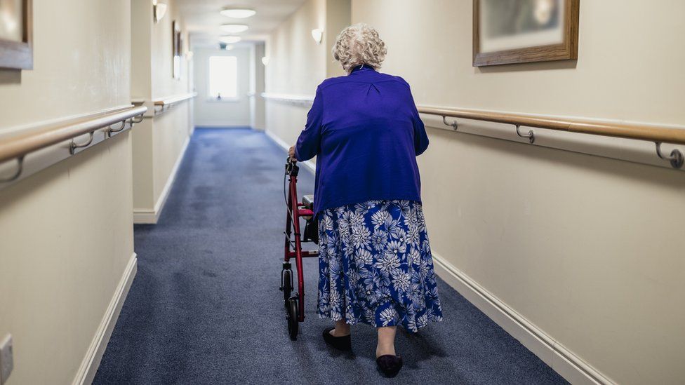 A woman walking down a corridor with the assistance of a walker