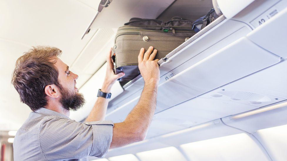 Man putting luggage in overhead locker on flight