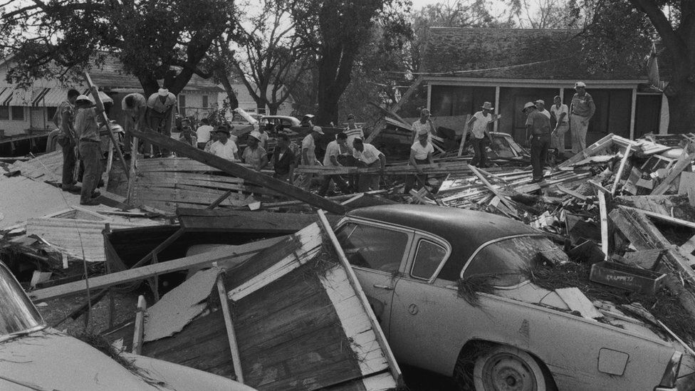 People climb over destroyed cars and collapsed buildings