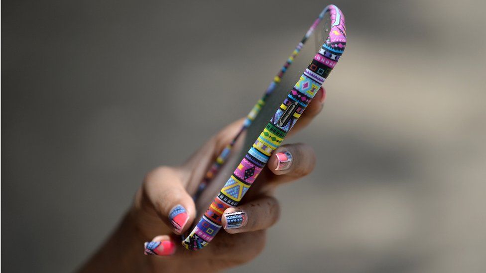 A hand with brightly painted nails holds a smartphone in a colourful case