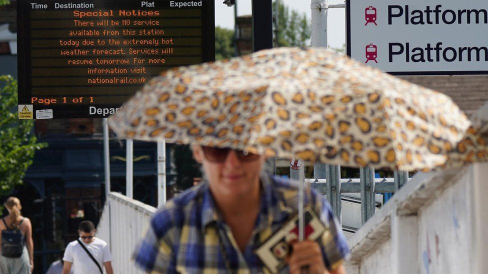 A person shelters from the sun near a sign showing cancelled rail services