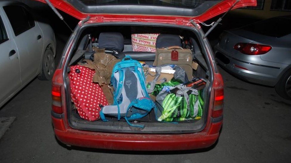 Un coche rojo lleno de bolsas saliendo del maletero