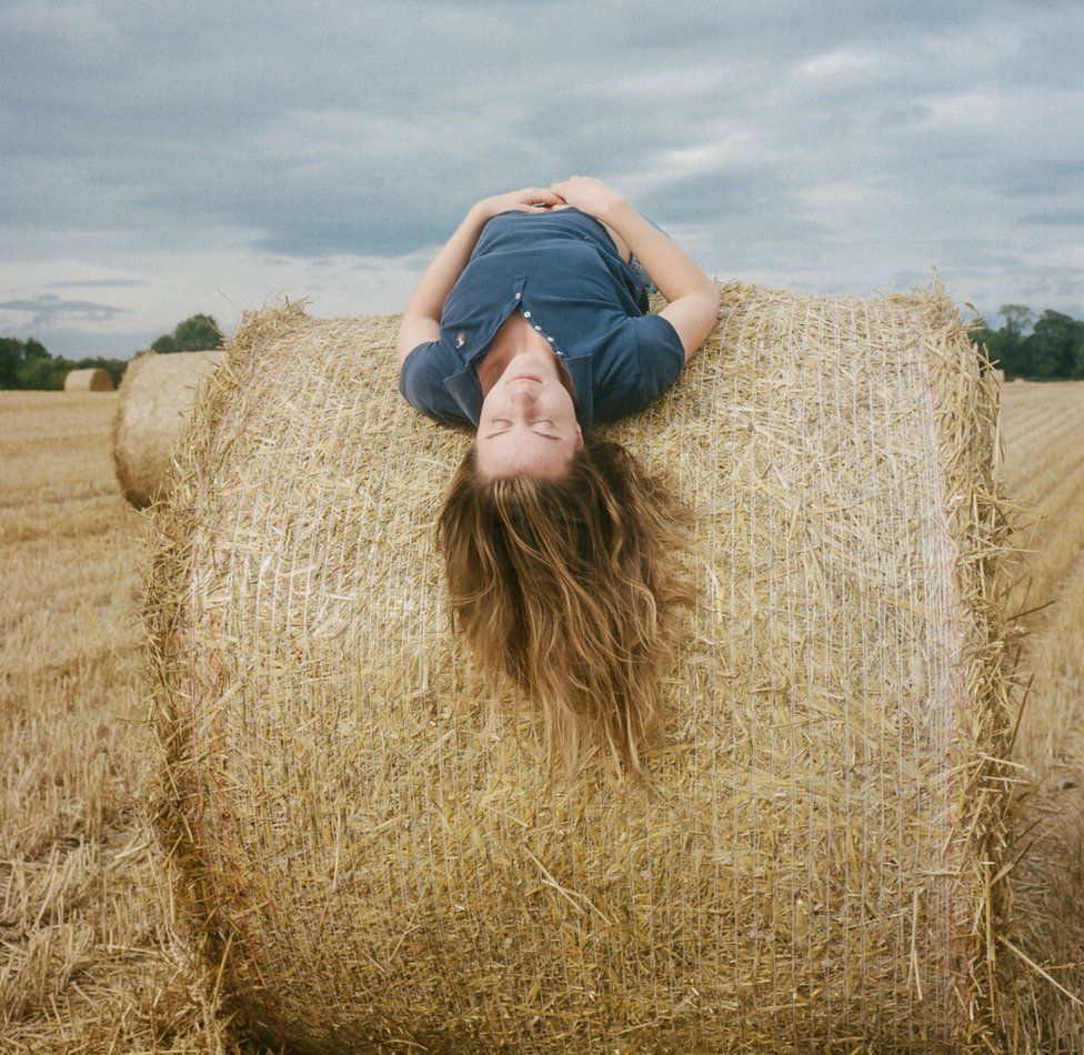 Poppy, a vet and farmer's daughter, lies across a hay stack at her home farm near Foulden in the Scottish Borders