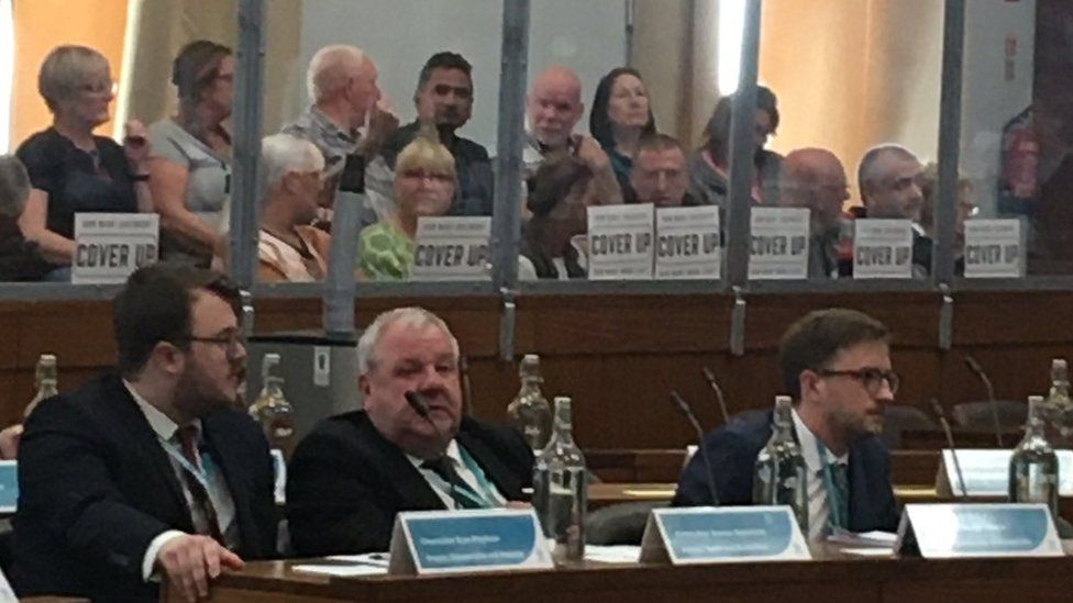 People holding up signs reading "cover up" at an Oldham Council meeting