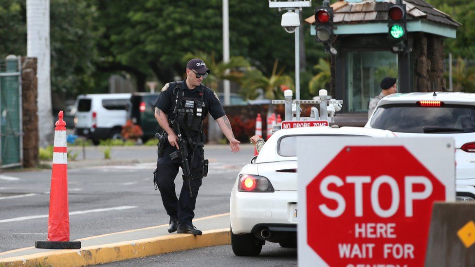 A guard armed with an assault rifle checks vehicles entering the Nimitz Gate entrance of Joint Base Pearl Harbor Hickam