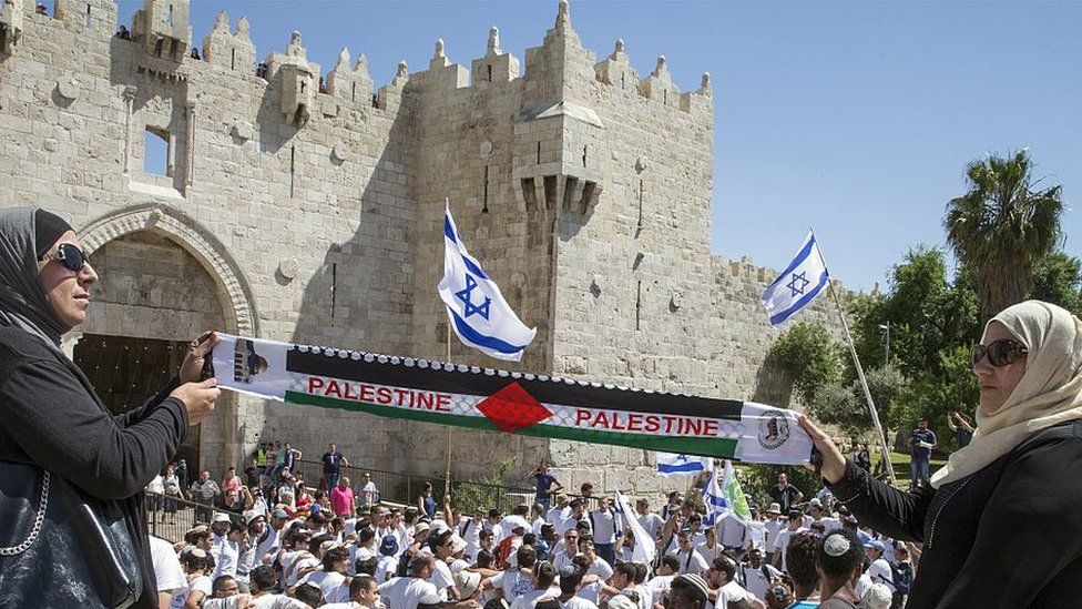 Palestinian women hold "Palestine" scarf as Israeli youth dance outside walls of Old City in Jerusalem (file photo)