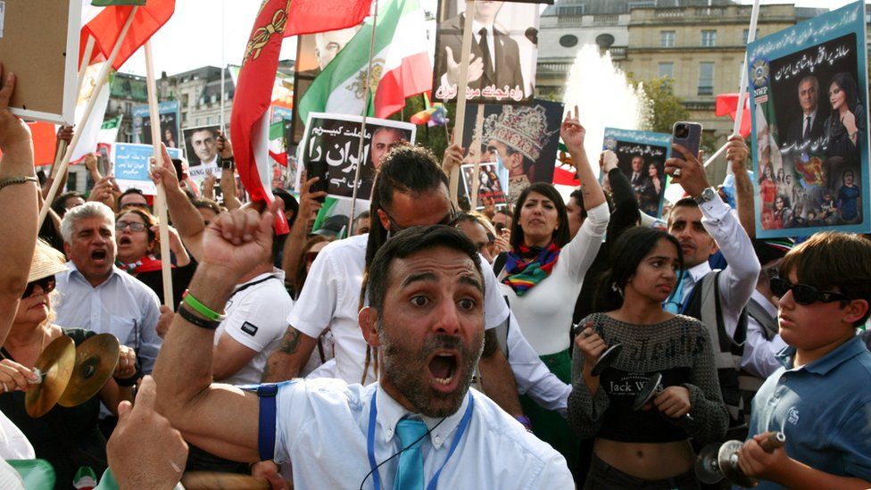 A man in a white shirt raises his fist in the air in Trafalgar Square in London