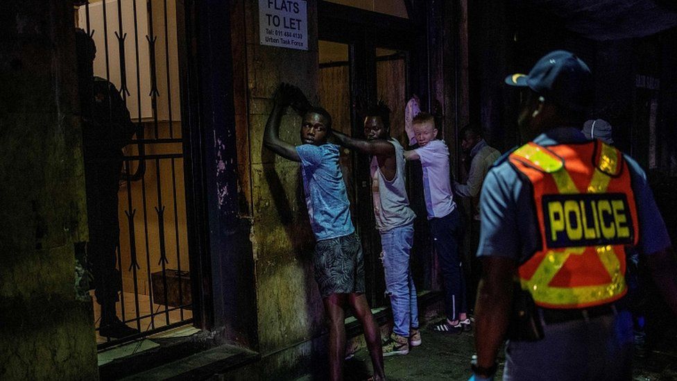 Suspects are lined up against a wall as a police officer wearing gloves arrests them because they defied the lockdown order during an operation in Johannesburg, on March 27, 2020