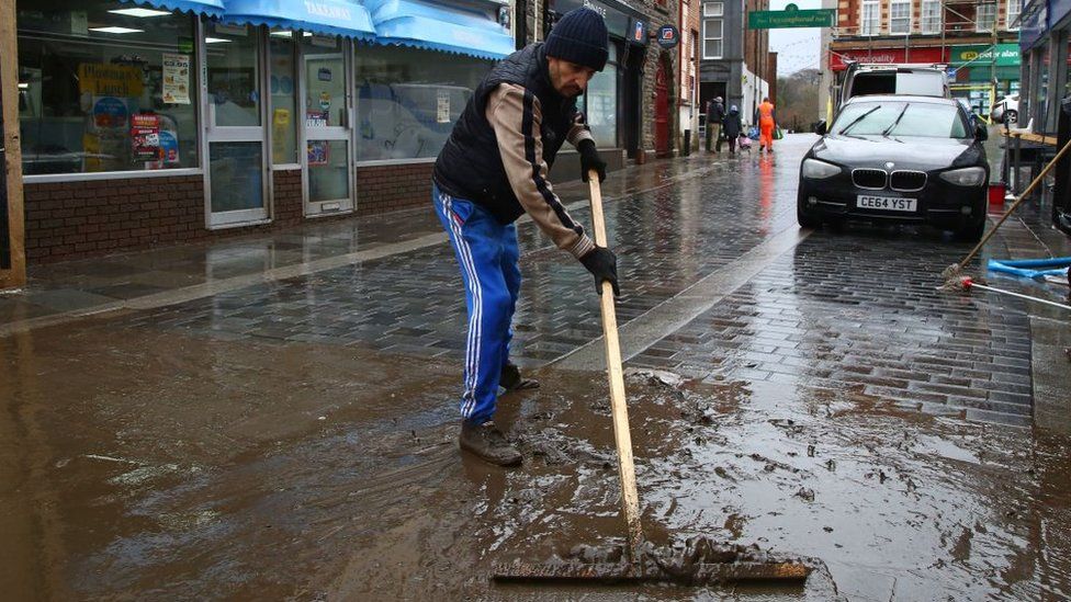Man cleans mud from street in Pontypridd, Rhondda Cynon Taf, after Storm Dennis flooding