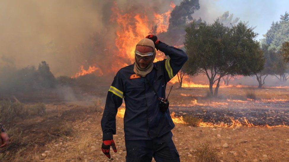 A firefighter walks next to rising flames as a wildfire burns near the village of Vati, on the island of Rhodes, Greece, July 25, 2023.