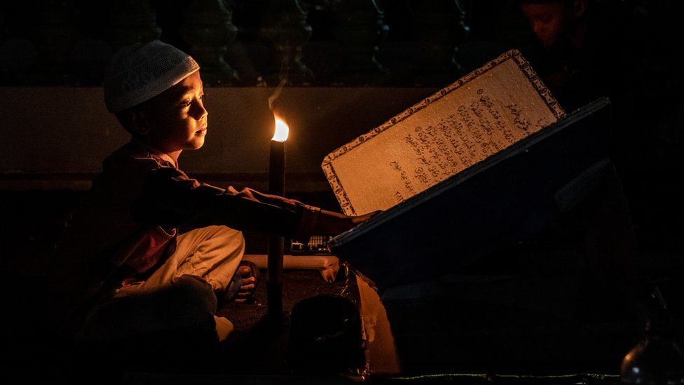 An Indonesian Muslim boy holds a torch while reading