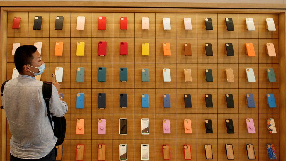 A man stands in front of a wall of iPhones cases in the new Apple flagship store on its opening day in Sanlitun in Beijing, China, July 17, 2020.