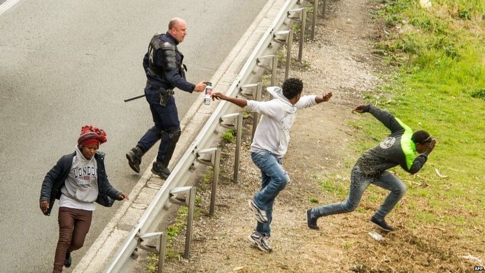 A police officer sprays tear gas to migrants trying to access the Channel Tunnel