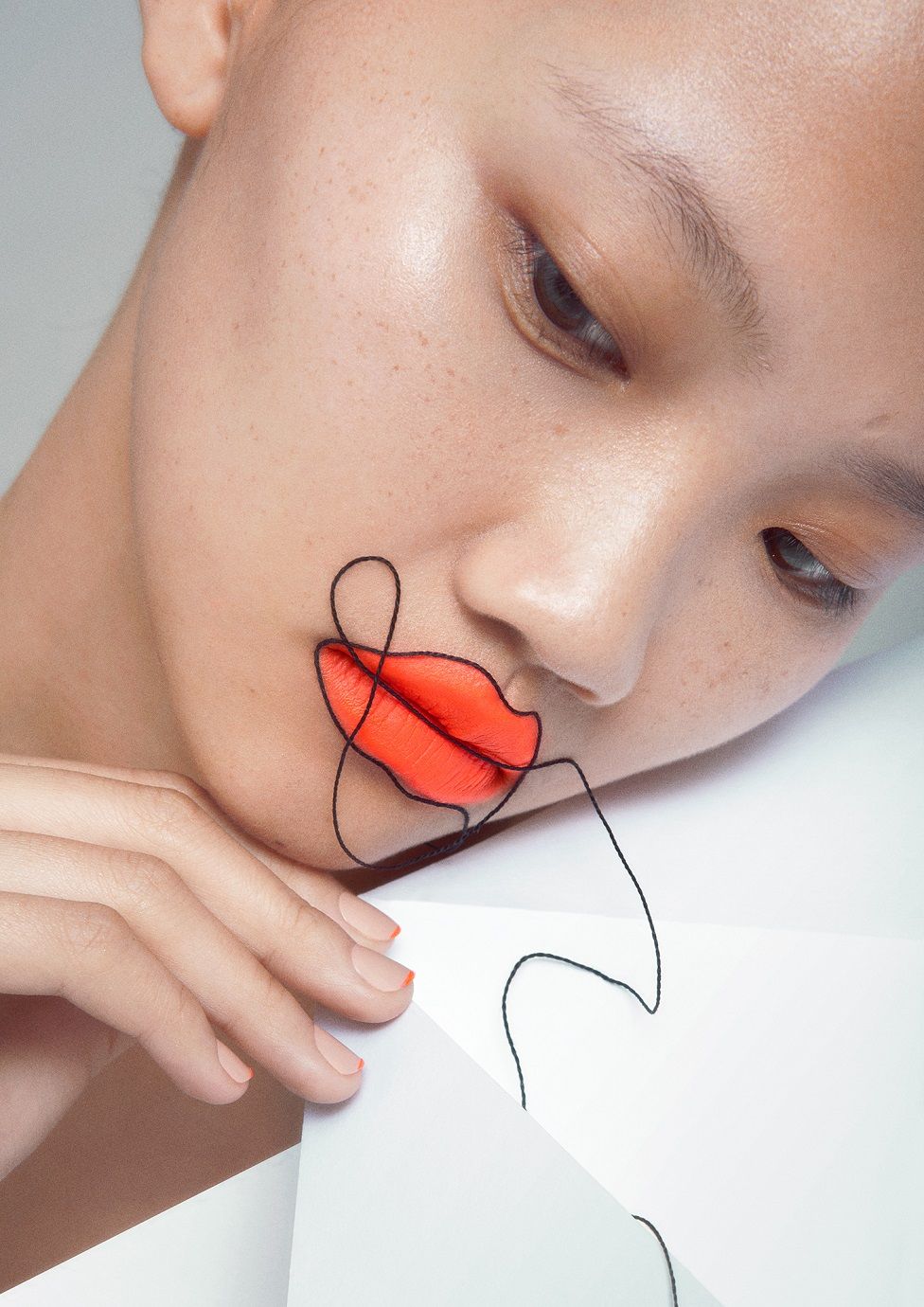 A model poses with bright lipstick and a thread running over her face and around the outline of her lips