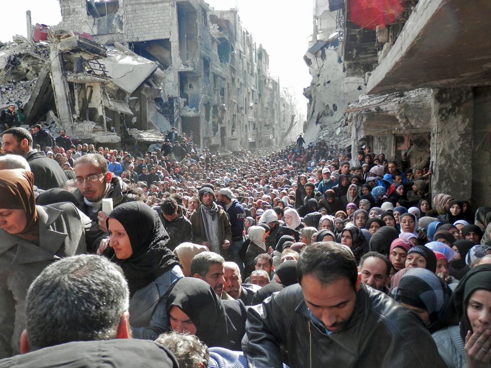 Residents wait in line to receive food aid distributed in the Yarmouk refugee camp on January 31, 2014 in Damascus, Syria