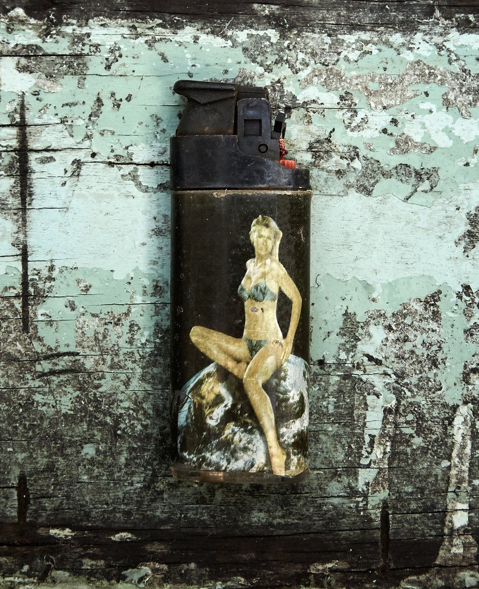 A scuffed and worn plastic lighter retrieved from the sea, featuring a bikini-clad woman sitting on an image of the Earth