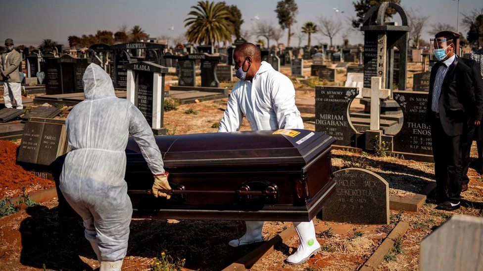 Relatives observe undertakers moving a casket containing the remains of a COVID-19 coronavirus patient during a funeral at the Avalon cemetery in Soweto, on July 24, 2020.