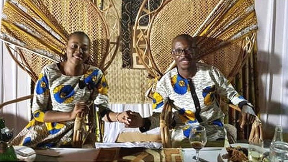 Arlene Agneroh and Jean-Felix Mwema Ngandu hold hands and smile as they sit side by side on throne-like chairs