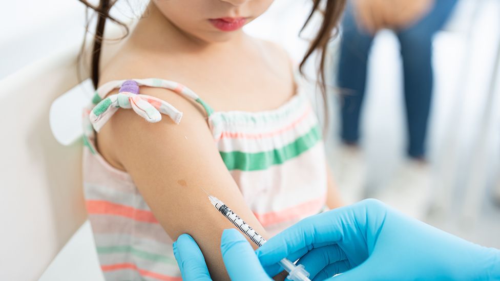 Anonymous child getting vaccine in upper right arm from healthcare professional wearing protective gloves