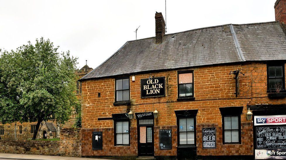 Two-storey brick pub with black window frames next to a churchyard