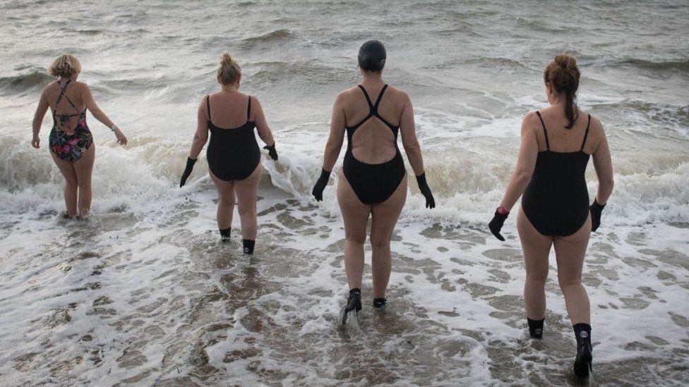 Four women walk into choppy sea waters.