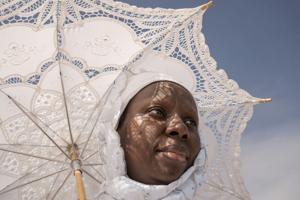 A woman dressed in white carries a matching white, lace parasol.