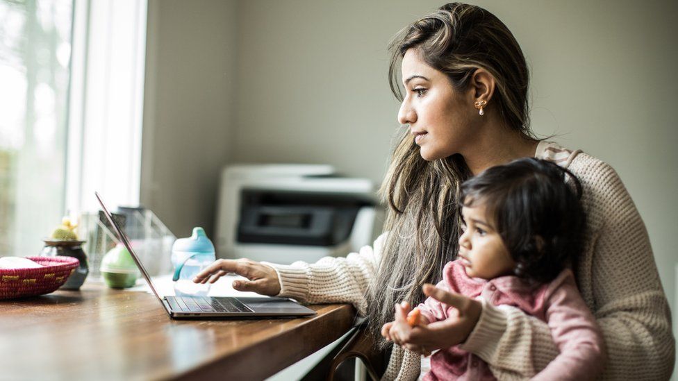A woman multi-tasking with her infant daughter while working at home