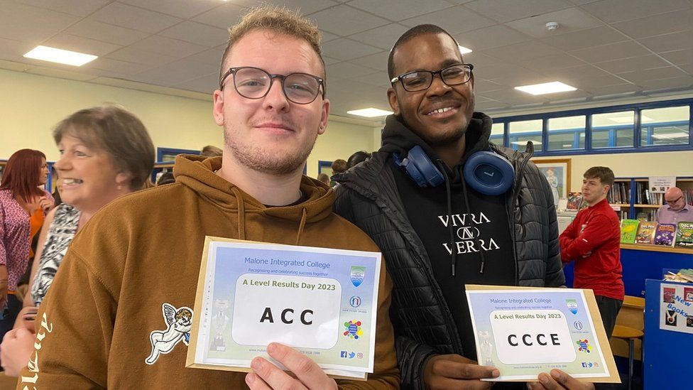 Two male students hold up their A-Level results slip.
