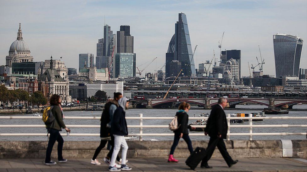 Pedestrians waling through Waterloo Bridge with the skyline of the City of London in the background