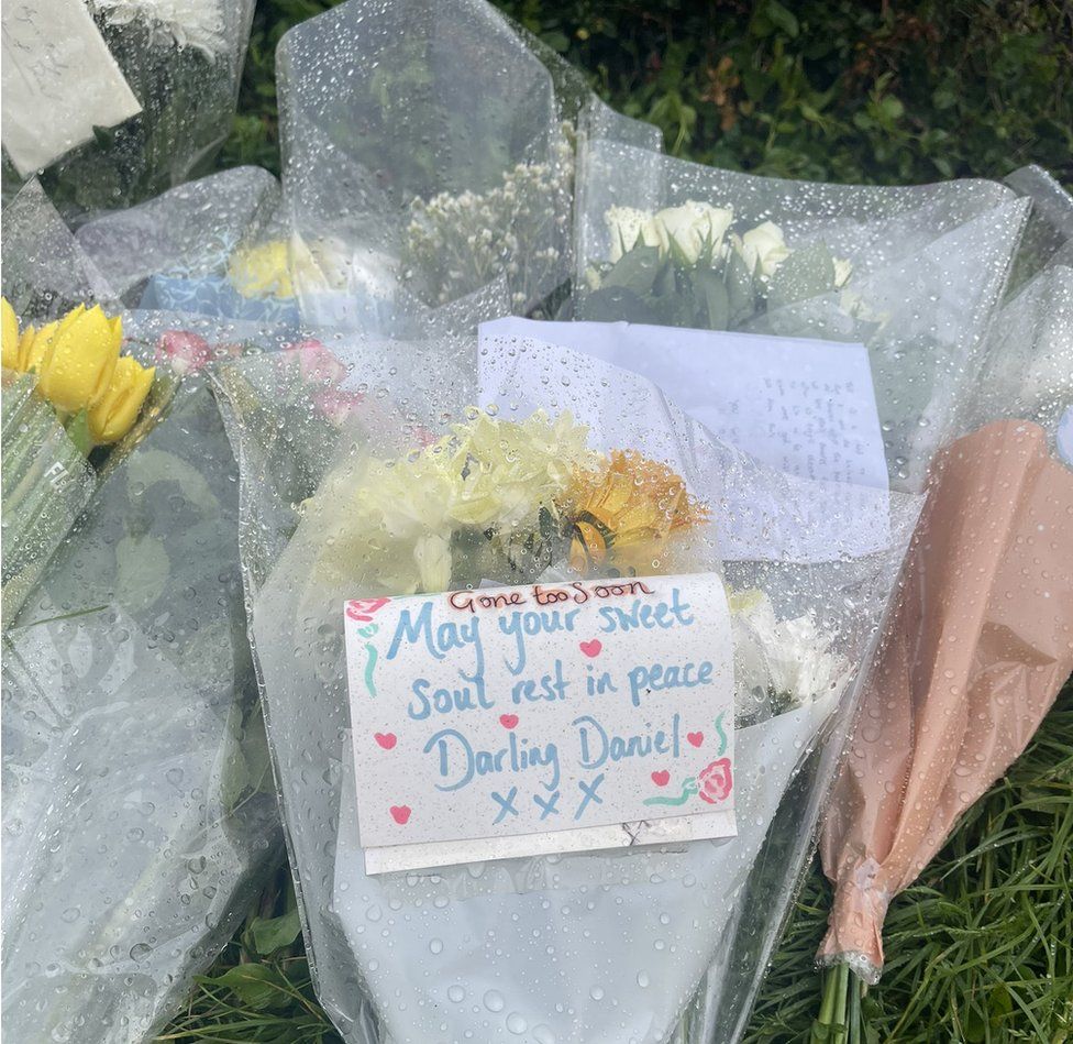 Flowers with a note which says 'gone too soon, may your sweet soul rest in peace darling Daniel'