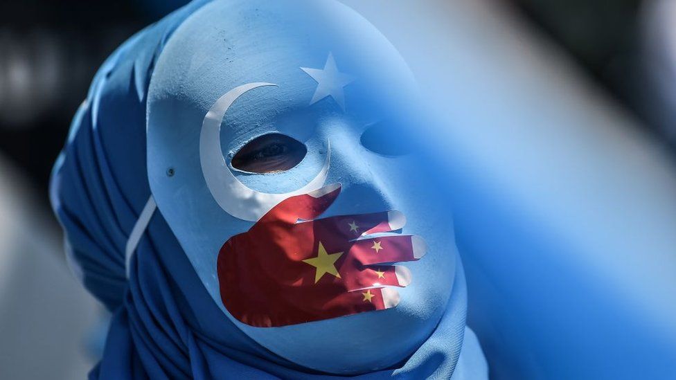 A pro-Uighur protester wears a mask painted with the colours of the East Turkestan flag and the Chinese flag